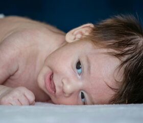 A newborn with a head of dark brown hair lying on his side.