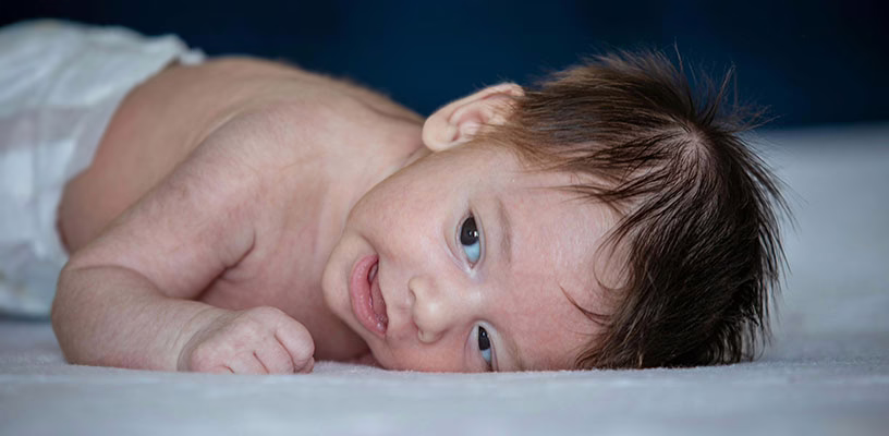 A newborn with a head of dark brown hair lying on his side.