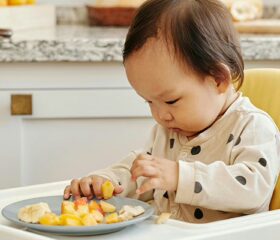 A baby who was started on the baby-led weaning approach sitting in a high chair, eating finger foods.