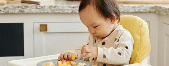 A baby who was started on the baby-led weaning approach sitting in a high chair, eating finger foods.