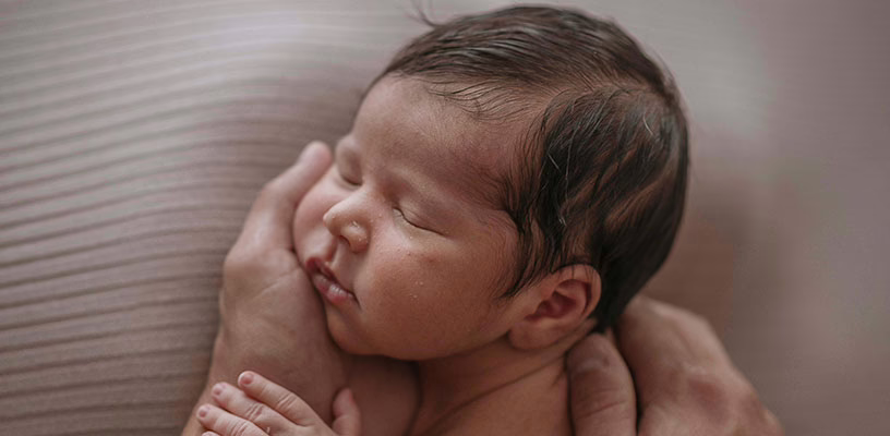 Adult holding her baby with her palm, trying not to touch the soft spot on her head.