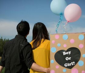 Couple sitting with a pink and blue balloon preparing for their gender reveal party.