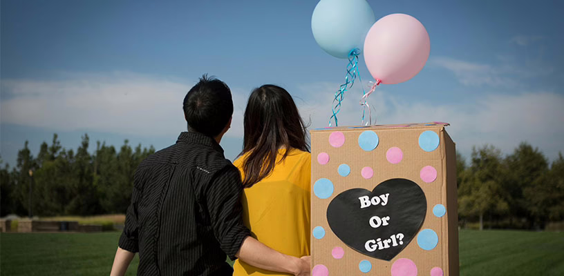 Couple sitting with a pink and blue balloon preparing for their gender reveal party.