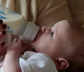 A baby lying in his mom's arms, drinking breast milk from a bottle his mom is holding.