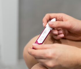 Woman on her period holding a pregnancy test and waiting for the result.