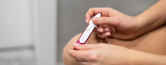 Woman on her period holding a pregnancy test and waiting for the result.