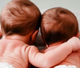 Two twin babies lying next to each other on their bellies.