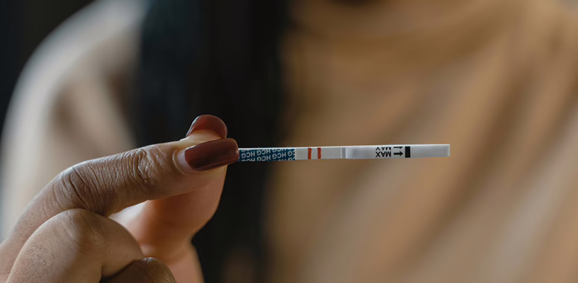 A close-up of a woman holding an hCG test strip.