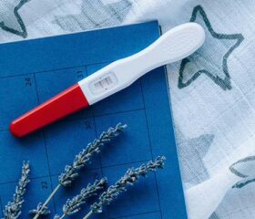 A positive pregnancy test on top of a calendar and a blue starry cloth.