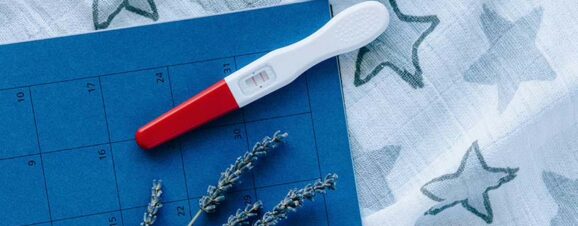 A positive pregnancy test on top of a calendar and a blue starry cloth.