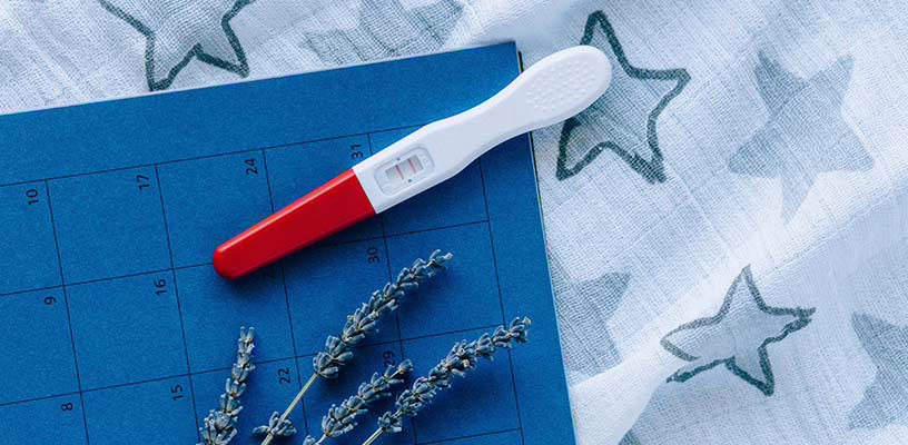 A positive pregnancy test on top of a calendar and a blue starry cloth.
