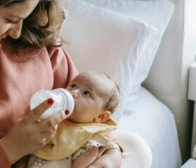 A mom holding her baby with one arm while feeding him formula.