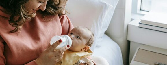 A mom holding her baby with one arm while feeding him formula.