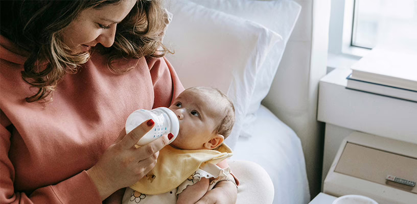 A mom holding her baby with one arm while feeding him formula.