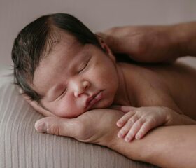 A newborn sleeping soundly with his head lying on his caregiver's palm.