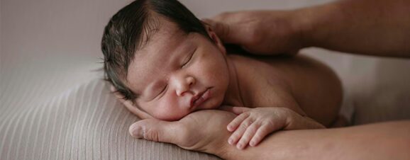 A newborn sleeping soundly with his head lying on his caregiver's palm.