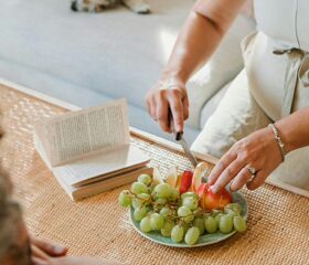 A pregnant woman slicing fruit on her coffee table.