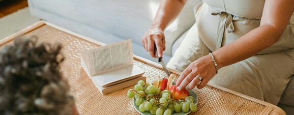 A pregnant woman slicing fruit on her coffee table.