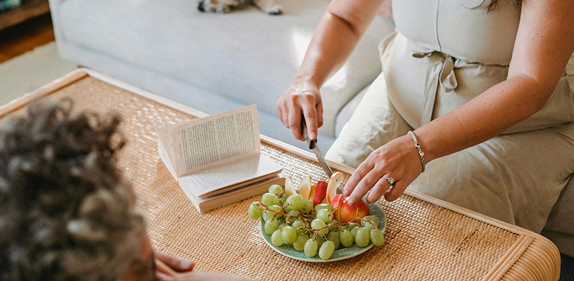 A pregnant woman slicing fruit on her coffee table.