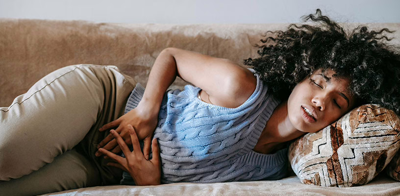 A woman with early pregnancy symptoms holding onto her stomach, lying on a couch.