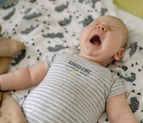 A fussy baby lying on his back with his eyes shut and mouth open as if crying.