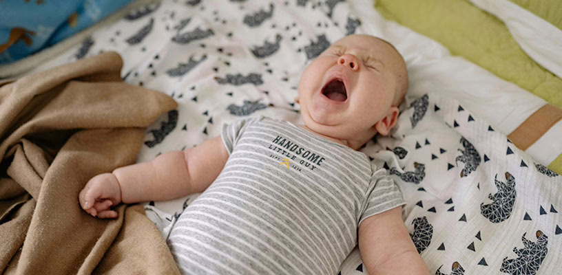 A fussy baby lying on his back with his eyes shut and mouth open as if crying.