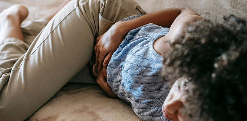 Woman with a possible threatened miscarriage lying on the bed holding her stomach.