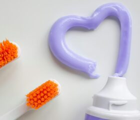 Two toothbrushes next to toothpaste that's shaped like a heart.