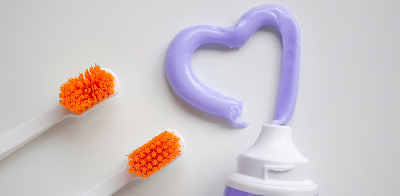Two toothbrushes next to toothpaste that's shaped like a heart.