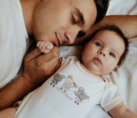 Dad lying on the bed with his newborn who has a short wake window.