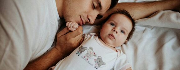 Dad lying on the bed with his newborn who has a short wake window.