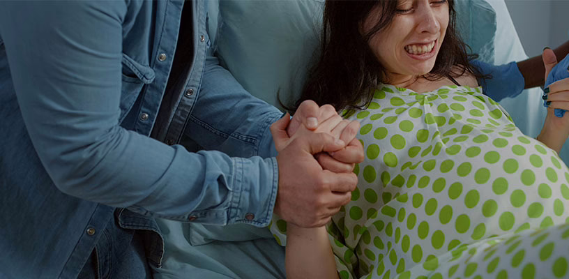 A woman having contractions holding on to her partner's and nurse's hands.