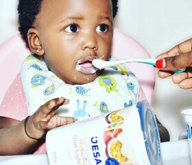 An adult feeding a spoonful of yogurt to a baby sitting in a highchair.