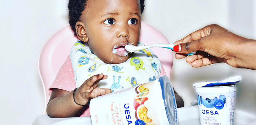 An adult feeding a spoonful of yogurt to a baby sitting in a highchair.