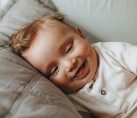 A smiling baby lying on his side on a big pillow.