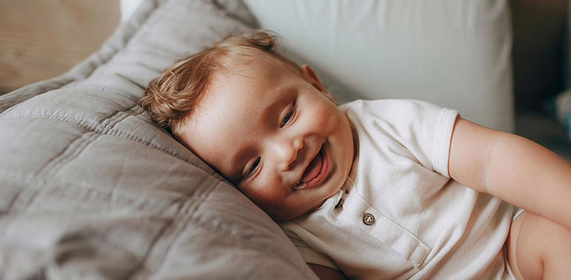 A smiling baby lying on his side on a big pillow.