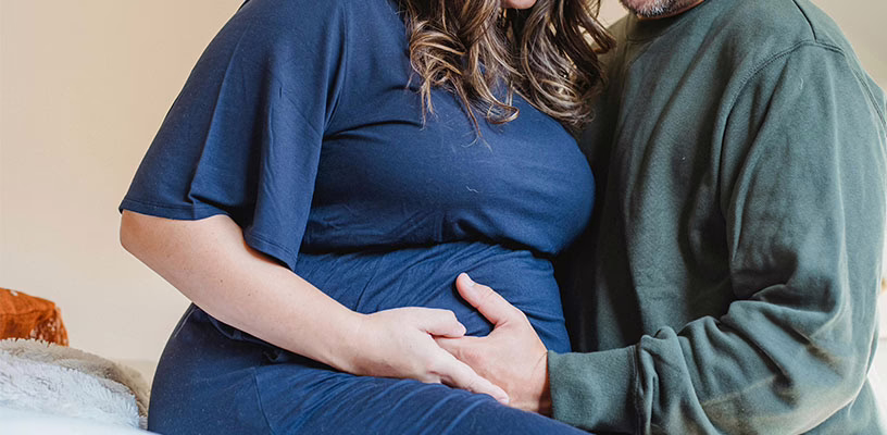 A pregnant woman and her partner place their hands on the woman's belly to feel their baby kicking.