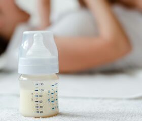 Baby bottle filled with milk in front of a mom playing with her baby.