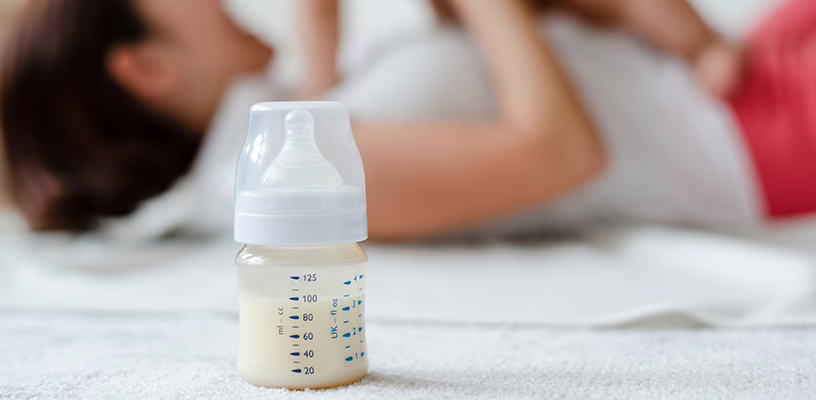 Baby bottle filled with milk in front of a mom playing with her baby.