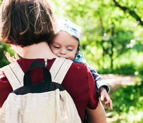 Mother carrying her baby while wearing a backpack-style diaper bag.