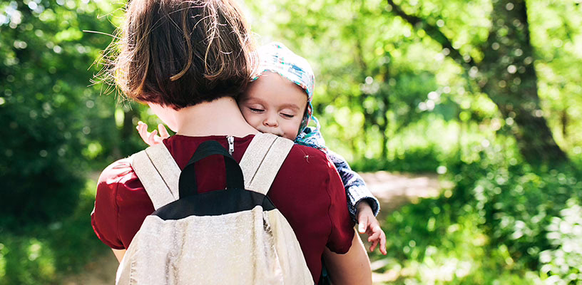 Mother carrying her baby while wearing a backpack-style diaper bag.