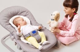 Toddler showing a stuffed toy to her younger sibling who's strapped into a baby lounger.