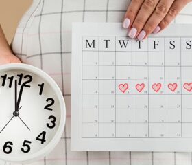 Woman holding a small clock and an ovulation calendar with her fertile window marked.