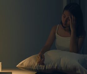 Woman sitting in bed, unable to sleep due to pregnancy insomnia.