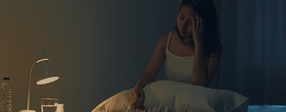 Woman sitting in bed, unable to sleep due to pregnancy insomnia.