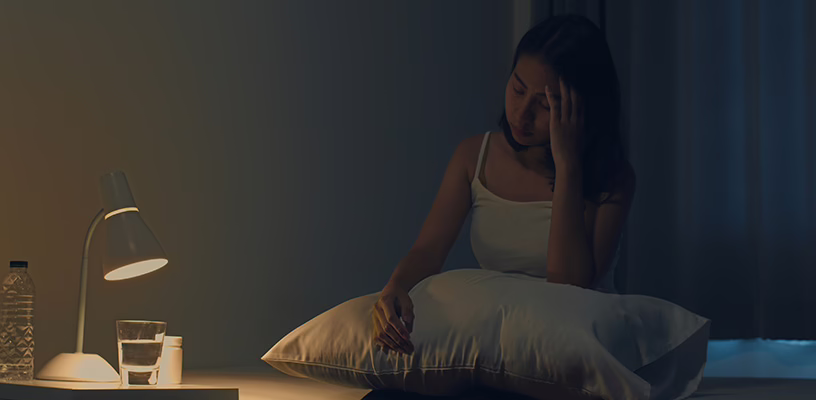 Woman sitting in bed, unable to sleep due to pregnancy insomnia.