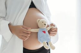Pregnant woman holding a teddy bear in front of her baby bump.