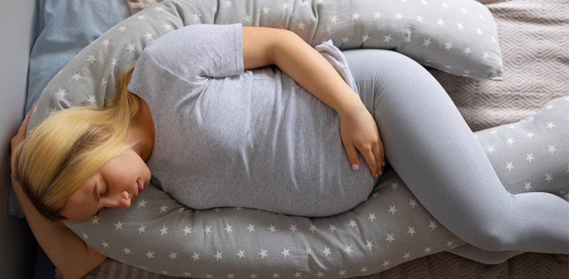 Woman lying on her side using a pregnancy pillow.