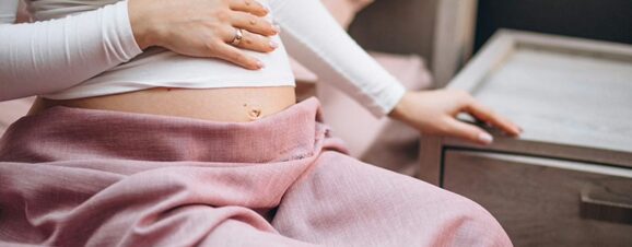 Pregnant woman placing her hand on her belly, feeling the symptoms of a retroverted uterus.