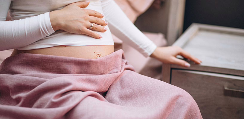Pregnant woman placing her hand on her belly, feeling the symptoms of a retroverted uterus.